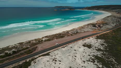 aerial-shot-of-a-van-driving-on-twilight-beach-road-near-esperance-with-the-ocean-in-the-background,-western-australia