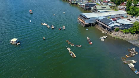 Traditional-Fishing-Boats-Transporting-Weeds-From-Stilt-House-Castro-Shore,-Chiloe-Island-Chile,-4K-Aerial-Drone