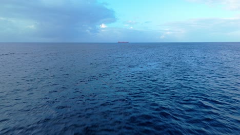 Deep-blue-ocean-water-with-cargo-tanker-on-horizon-at-edge-of-wispy-clouds,-aerial-drone-texture