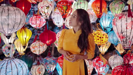 Woman-in-yellow-Ao-Dai-admiring-colorful-lanterns-at-night-in-Hoi-An,-Vietnam,-vibrant-culture-scene