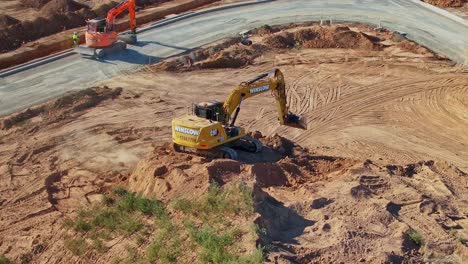 Yarrawonga,-Victoria,-Australia---8-March-2024:-Aerial-around-an-excavator-preparing-a-bucket-of-dirt-to-load-a-trip-truck-at-Silverwoods-Estate-in-Yarrawonga