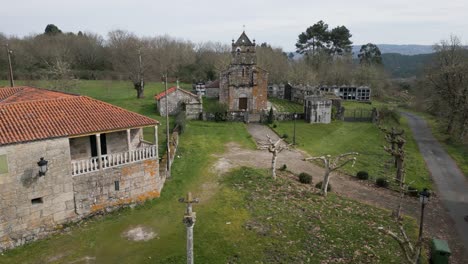 Aerial-dolly-above-empty-grass-field-to-front-of-moss-covered-church,-Church-of-Santa-Maria-de-Vilela-in-Punxin-Ourense-Spain