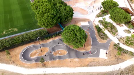 Aerial-View-of-Kids-Scootering-in-Skatepark-Amidst-Green-Trees