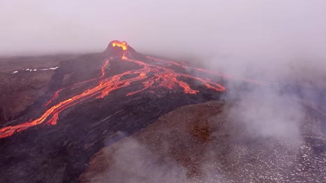 A-high-resolution-4K-drone-captures-cinematic-aerial-footage,-presenting-unique-wide-angle-shots-of-a-landscape-featuring-a-volcano-and-flowing-lava,-with-swirling-fog-enveloping-the-scene