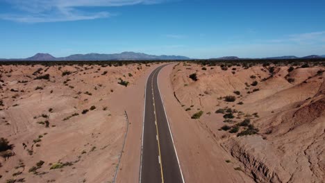 Aerial-rises-over-highway-curve-in-vast-red-rock-badland-landscape