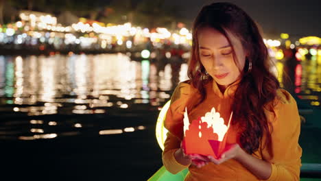 Vietnamese-woman-in-yellow-dress-prays-with-paper-candle-on-river-boat-at-night-in-Hoi-An,-Vietnam-in-slow-motion