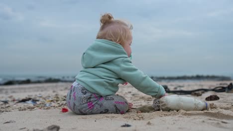 A-blonde-baby-girl-picking-up-a-plastic-bottle-on-the-beach-and-throwing-it-at-the-camera