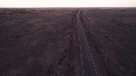 Sunset-drone-shot-of-a-vehicle-driving-down-a-remote-desert-highway