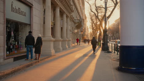 Sunset-on-Andrássy-Avenue-Budapest-Hungary,-People-walking-on-the-famous-Hungarian-luxury-shopping-street,-European-architecture,-tourist-attraction,-famous-landmarks,-beautiful-warm-sunbeam,-winter
