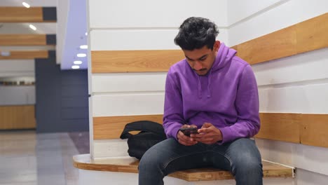 Asian-man-with-short-black-hair-uses-smartphone-indoors-sitting-in-the-corner
