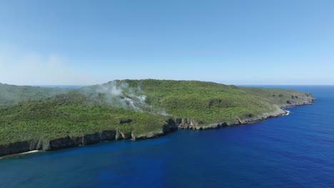 Aerial-approaching-shot-of-wildfire-on-tropical-island-with-blue-sea-water