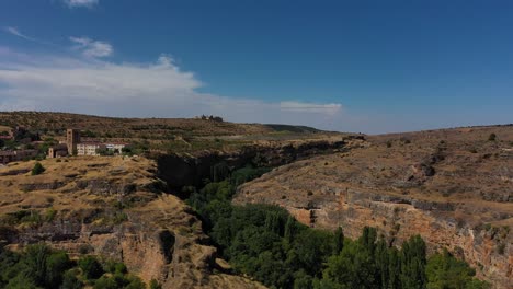 Rückwärtsflug---Aufstieg-Sofort-über-Eine-Kalksteinschlucht-Mit-Bäumen-Im-Verlauf-Der-Schlucht-Und-Visualisierung-Einer-Stadt-Mit-Einem-Turm-An-Einem-Sommermorgen-Mit-Blauem-Himmel-Segovia-Spanien