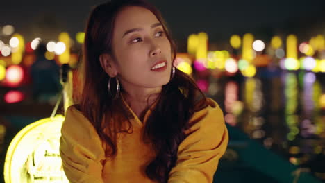 Close-up-of-attractive-Vietnamese-woman-on-boat-with-blurred-background-looking-at-night-river,-Hoi-An,-Vietnam