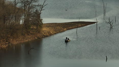 Two-people-fishing-from-a-boat-on-Lake-Flint-Creek-near-Lake-Swepco,-Arkansas,-on-an-overcast-day