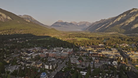 Banff-AB-Canada-Aerial-v23-flyover-town-center-and-Bow-river-capturing-residential-houses,-horse-stables-and-sunlight-on-forested-valley-and-mountain-ranges---Shot-with-Mavic-3-Pro-Cine---July-2023