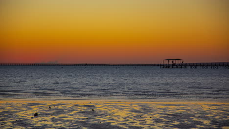 Beautiful-sunrise-on-the-horizon-on-the-beach-with-a-pier-in-the-sea-and-small-islands-in-the-background