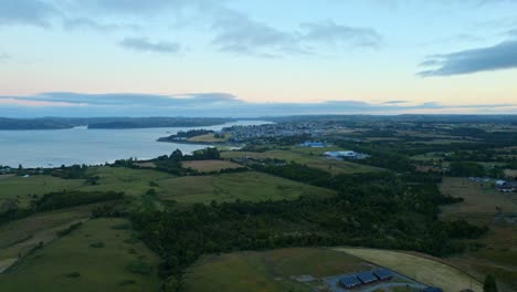 Drone-Aéreo-Sobre-El-Paisaje-De-La-Isla-Patagónica-Chilena-De-Chiloé,-Fondo-Chonchi,-Medio-Ambiente,-Naturaleza-De-América-Del-Sur,-Bahía-Azul-Con-Horizonte-Al-Atardecer