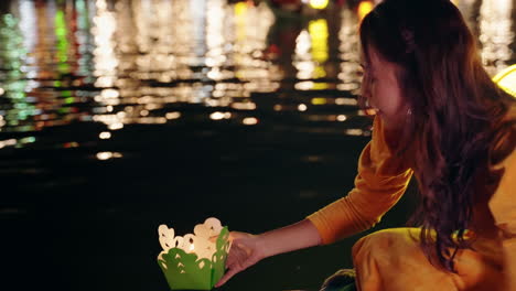 Slow-motion-of-Vietnamese-woman-in-traditional-dress-putting-paper-candle-boat-on-river-at-night-in-Hoi-An,-Vietnam