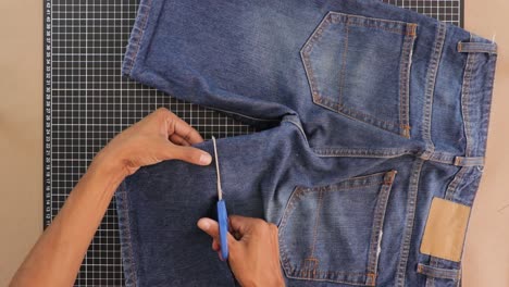 Person-remodeling-and-cutting-short-trousers-with-scissors