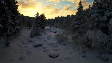 Drone-Flies-Through-Snow-Covered-Forest-Creek-At-Dusk-In-Lapland,-Finland,-Arctic-Circle