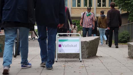 People-move-by-voting-station-sign,-election-day-in-Stockholm,-Sweden