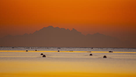 Wunderschöne-Zeitrafferaufnahmen-Des-Meeres-Mit-Buntem-Himmel-Bei-Sonnenuntergang,-Im-Hintergrund-Die-Silhouette-Eines-Berges