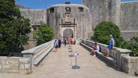 Vrata-Od-Pila,-Puente-Y-Puerta-De-Entrada-Al-Casco-Antiguo-De-Dubrovnik,-Croacia,-Turistas-Caminando-En-Un-Día-Soleado-De-Verano