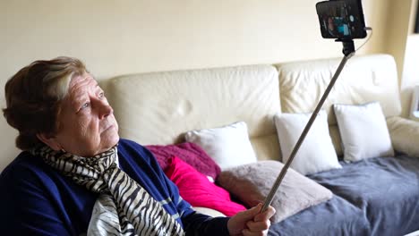 Elderly-woman-using-a-selfie-stick-with-smartphone-at-home