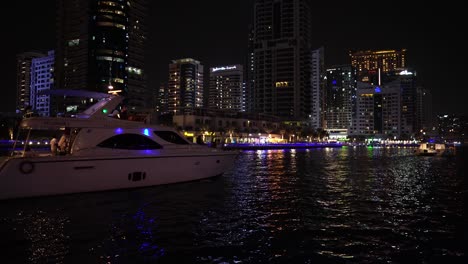 Yacht-In-Der-Wasserstraße-Der-Dubai-Marina-Bei-Nacht,-Lichter-Und-Uferpromenade