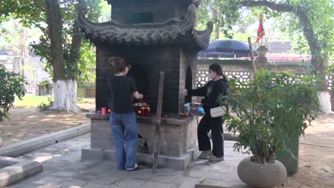 Zwei-Vietnamesische-Frauen-Führen-Im-Quan-Thanh-Tempel-In-Hanoi-Ein-Ritual-Mit-Räucherpapier-Durch