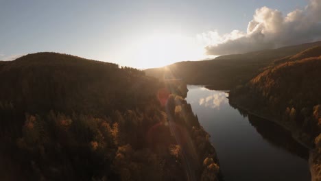 Filmische-Luftaufnahme-Einer-Geraden-Straße-Entlang-Eines-Malerischen-Staudamms,-Umgeben-Von-üppigen-Herbstbäumen