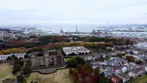 A-historic-castle-surrounded-by-autumn-foliage-and-urban-backdrop,-overcast,-aerial-view