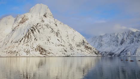 Kayakista-Pasando-Lentamente-Hacia-Reinefjorden-En-Lofoten,-La-Montaña-Olstinden-Al-Fondo