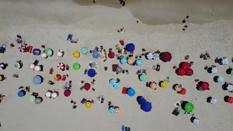 Drone-Con-Cámara-90-Grados-Abajo-Con-Movimiento-Lateral-Filmando-Varias-Sombrillas-Coloridas-Y-Personas-En-La-Playa-De-Ipanema,-Brasil