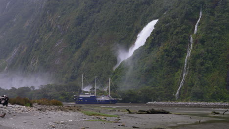 4K-Aufnahmen-Eines-Dreimasters,-Der-Vor-Einem-Wasserfall-Im-Milford-Sound-In-Den-Hafen-Einläuft-–-Piopiotahi,-Neuseeland