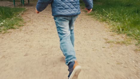 A-boy,-a-child-in-jeans,-sneakers-and-a-quilted-jacket-runs-on-a-gravel-road-in-the-park