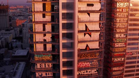 Aerial-close-up-descending-shot-of-the-Oceanwide-Plaza-graffiti-skyscrapers-at-sunset-in-downtown-Los-Angeles,-California