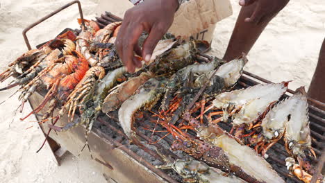 Lobsters-and-prawns-cooked-on-small-grill-on-the-beach,-local-man-catches-fish-with-his-hand,-Zanzibar,-Tanzania,-shot-at-30-fps