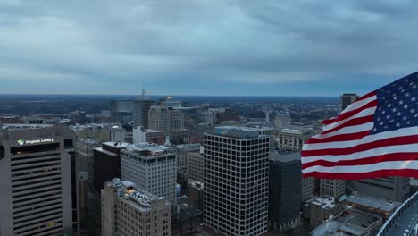 Aerial-close-up-of-an-American-flag-waving-over-a-city-skyline