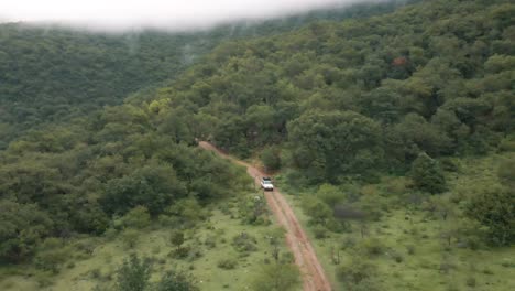 White-Cherokee-truck-driving-through-the-forest-with-misty-mountain-weather,-aerial-drone-shot