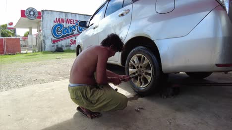 Local-car-mechanic-replacing-rear-tire-without-wearing-clothes-on-top,-handheld