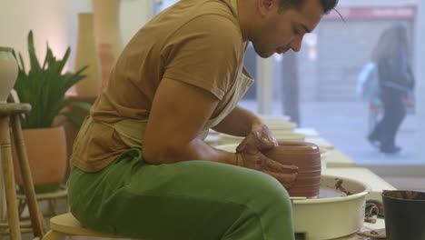 Creative-male-potter-sitting-moulding-and-working-clay-pottery-on-turntable-in-studio-workshop