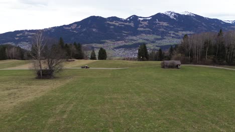 Drone-shot-of-Tractor-driving-in-scenic-landscape-with-snowy-mountain-landscape-in-background