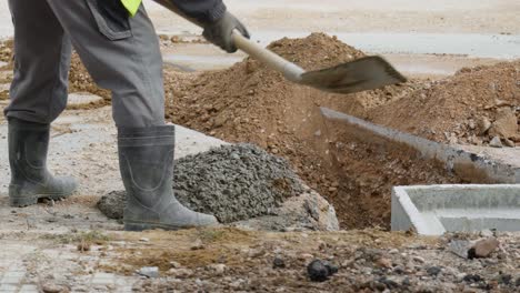 Männlicher-Bauarbeiter-Gießt-Zementbeton-Mit-Schaufel-Um-Vorgefertigte-Betongrube-Für-Neues-Drainagerohrsystem-Für-Straßen