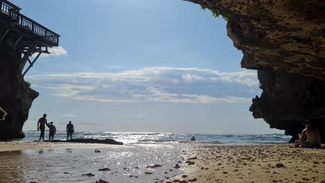 Bali-Island-Indonesia,-Surfers-With-Surf-Board-Walking-on-Beach-Under-Uluwatu-Cliffs-on-Sunny-Day