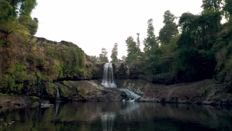 Die-Drohnenkamera-Bewegt-Sich-Aus-Der-Luft-Vorwärts,-Wo-Ein-Großer-Wasserfall-Fällt-Und-Ein-Großer-Fluss-Sichtbar-Ist-Und-Er-Von-Hohen-Bäumen-Umgeben-Ist