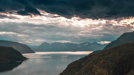 Strahlen-Der-Untergehenden-Sonne-Durchdringen-Die-Dichten-Gewitterwolken,-Die-über-Dem-Ruhigen-Fjord-Wirbeln