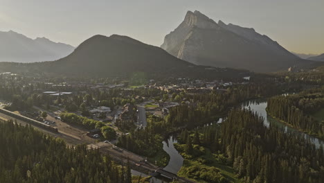 Banff-AB-Canada-Aerial-v33-cinematic-flyover-capturing-scenic-landscape-of-train-crossing-quaint-town-by-the-Bow-river-and-Rundle-mountain-ranges-at-sunrise---Shot-with-Mavic-3-Pro-Cine---July-2023