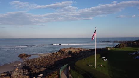 Ogunquit-Maine-USA-drone-fly-close-to-United-States-flag-revealing-scenic-seascape-coastline-during-sunny-day