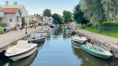 Menschen-Gehen-An-Booten-Vorbei,-Die-An-Flussufern-In-Der-Stadt-Trosa-In-Schweden-Angedockt-Sind